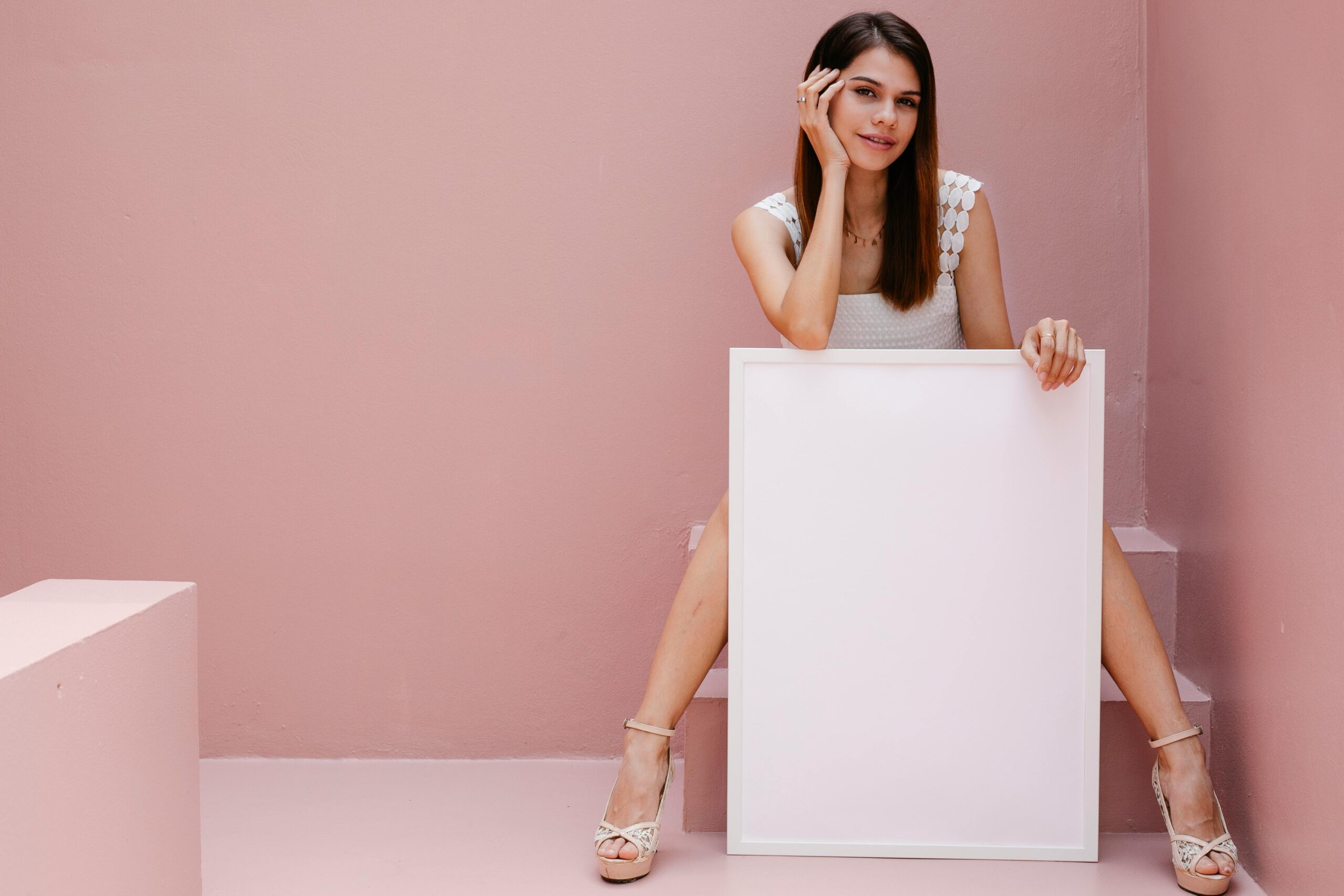 Young woman sitting with blank poster in bright, modern setting, ideal for mockups.